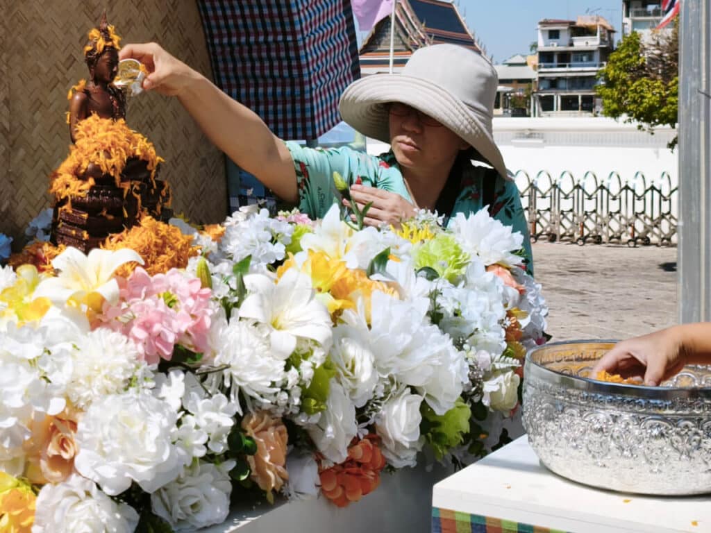 A woman waters a Buddha statue during Songkran